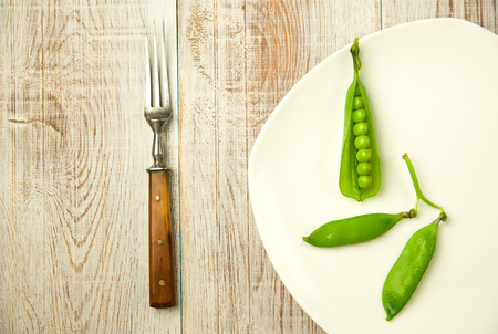 Green pea pods and fork on the white plate.の写真素材