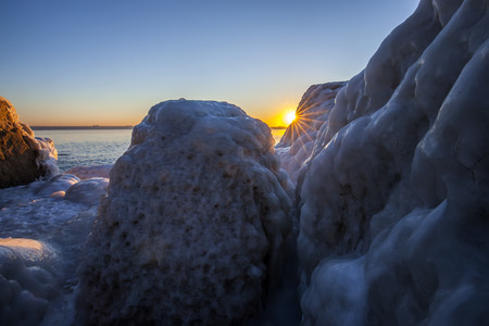 Sunrise by the sea in winter.The rocks were covered with snow and iceの写真素材