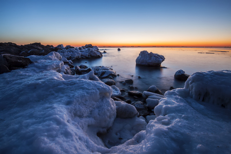 Sunrise by the sea in winter.The rocks were covered with snow and iceの写真素材