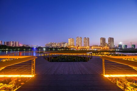 The city by the river is at night, The wooden walkway by the river and the night view of the cityの写真素材