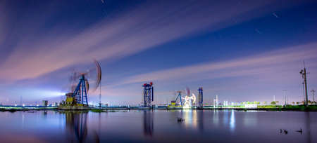 Oil field site, in the evening, oil pumps are running, The oil pump and the beautiful sunset reflected in the water, the silhouette of the beam pumping unit in the evening.の写真素材