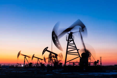 Oil field site, in the evening, oil pumps are running, Silhouette of beam pumping unitの写真素材