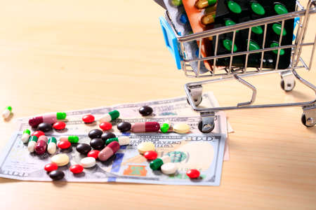 Pharmacy background. Pills on a banknote isolated on a white background. Different types of capsules on dollars banknote. Money and pharmaceutical industry.の写真素材