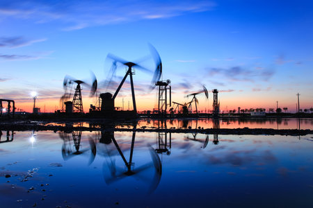 Oil field site, in the evening, oil pumps are running, The oil pump and the beautiful sunset reflected in the water, the silhouette of the beam pumping unit in the evening.の写真素材