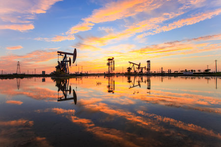 Oil field site, in the evening, oil pumps are running, The oil pump and the beautiful sunset reflected in the water, the silhouette of the beam pumping unit in the evening.の写真素材