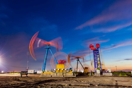 Oil field site, in the evening, oil pumps are running, The oil pump and the beautiful sunset reflected in the water, the silhouette of the beam pumping unit in the evening.の写真素材