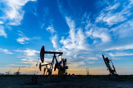 Oil field site, in the evening, oil pumps are running, The oil pump and the beautiful sunset reflected in the water, the silhouette of the beam pumping unit in the evening.の写真素材