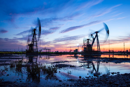Oil field site, in the evening, oil pumps are running, The oil pump and the beautiful sunset reflected in the water, the silhouette of the beam pumping unit in the evening.の写真素材