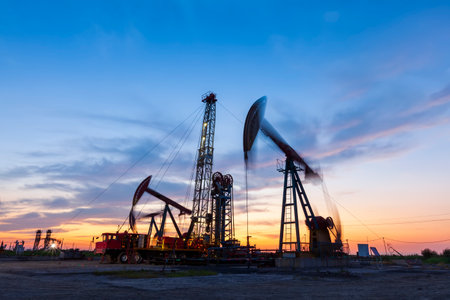 Oil field site, in the evening, oil pumps are running, The oil pump and the beautiful sunset reflected in the water, the silhouette of the beam pumping unit in the evening.の写真素材