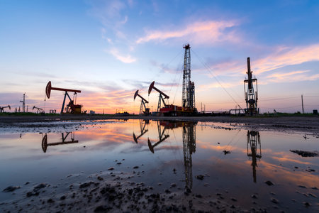 Oil field site, in the evening, oil pumps are running, The oil pump and the beautiful sunset reflected in the water, the silhouette of the beam pumping unit in the evening.の写真素材