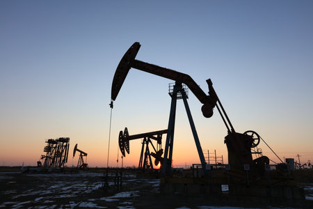 Oil field site, in the evening, oil pumps are running, Silhouette of beam pumping unitの写真素材