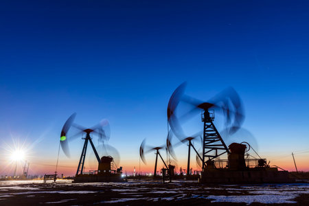 Oil field site, in the evening, oil pumps are running, Silhouette of beam pumping unit