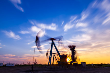 Oil field site, in the evening, oil pumps are running, The oil pump and the beautiful sunset reflected in the water, the silhouette of the beam pumping unit in the evening.の写真素材