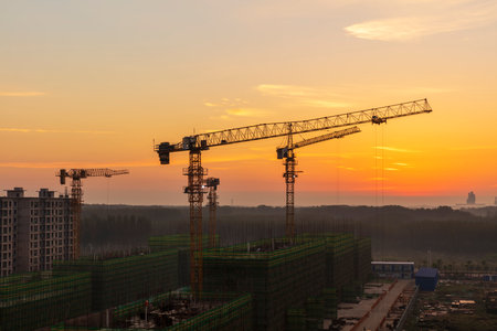 The construction site is in the morning. In the morning, the tower hangs over the construction site, , Tower cranes build residential buildingsの写真素材