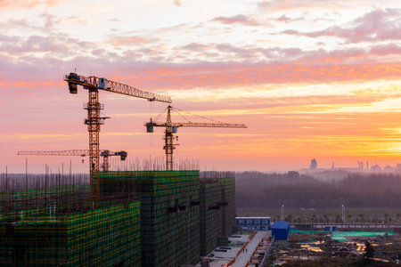 The construction site is in the morning. In the morning, the tower hangs over the construction site, , Tower cranes build residential buildingsの写真素材