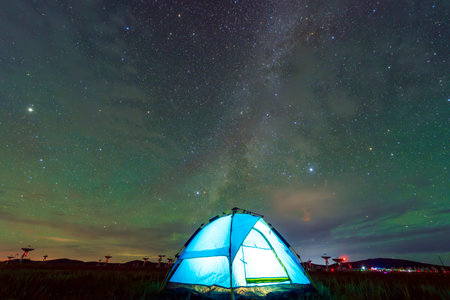 At night, the blue tent is on the grassland. The tent is under the starsの写真素材
