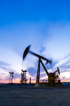 Oil field site, in the evening, oil pumps are running, The oil pump and the beautiful sunset reflected in the water, the silhouette of the beam pumping unit in the evening.の写真素材