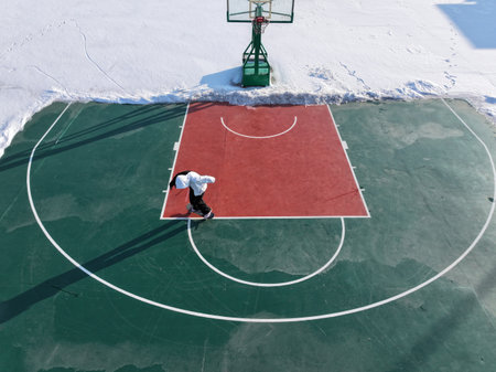 In winter, a boy is skateboarding on a basketball court, which is surrounded by snowの写真素材