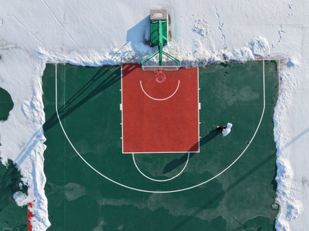In winter, a boy is skateboarding on a basketball court, which is surrounded by snowの写真素材