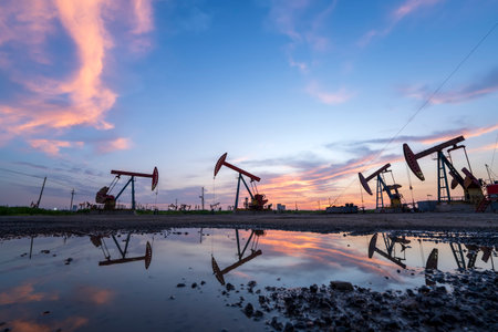 Oil field site, in the evening, oil pumps are running, The oil pump and the beautiful sunset reflected in the water, the silhouette of the beam pumping unit in the evening.の写真素材