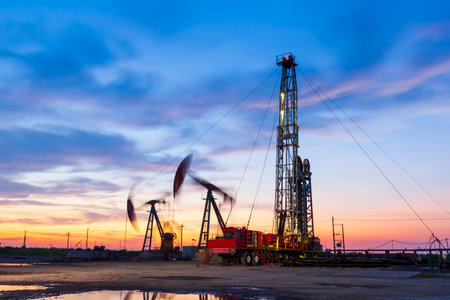 Oil field site, in the evening, oil pumps are running, The oil pump and the beautiful sunset reflected in the water, the silhouette of the beam pumping unit in the evening.の写真素材