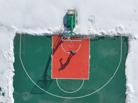 In winter, a boy was playing basketball on a basketball court, which was surrounded by snow