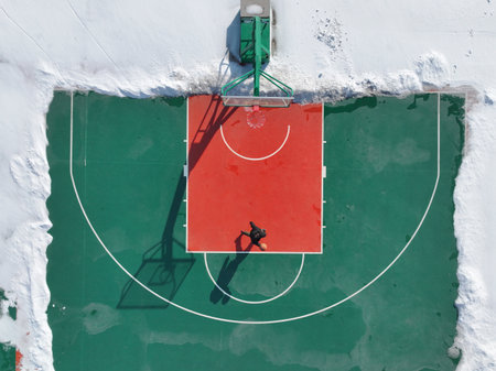 In winter, a boy was playing basketball on a basketball court, which was surrounded by snowの写真素材