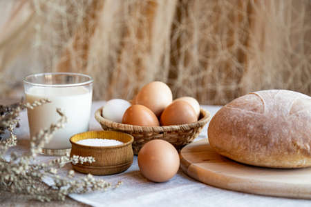 Still life bread eggs salt and milk on wooden plates on a background in warm colorsの写真素材