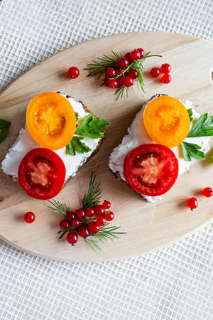Sandwiches with tomato and herbs and berries on a wooden cutting boardの写真素材