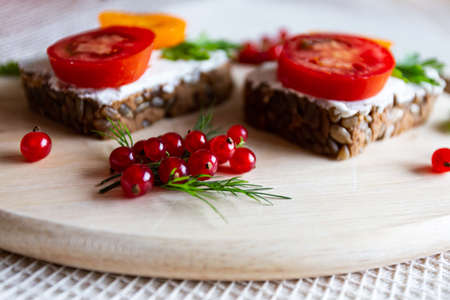 Sandwiches with tomato and herbs and berries on a wooden cutting boardの写真素材