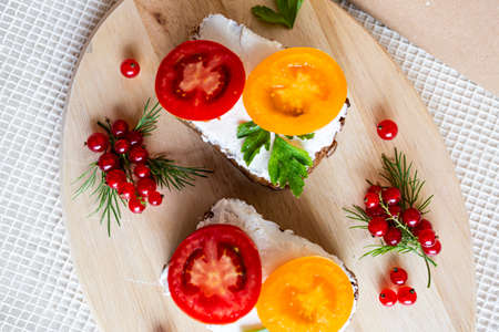 Sandwiches with tomato and herbs and berries on a wooden cutting boardの写真素材