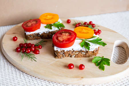 Sandwiches with tomato and herbs and berries on a wooden cutting boardの写真素材