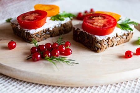 Sandwiches with tomato and herbs and berries on a wooden cutting boardの写真素材