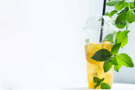 Green tea with iced lemon and lemon balm in a plastic glass on a white backgroundの写真素材