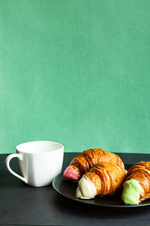 Breakfast. Cup of coffee and croissants on black plate on colored background with copy spaceの写真素材