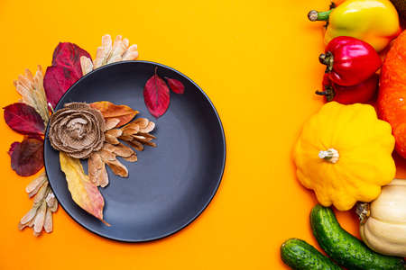 Black plate and in autumn leaves and vegetables on a yellow background. Festive autumn concept.の写真素材