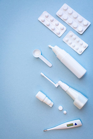 White thermometer, pills, vials with nasal spray and throat spray on blue background