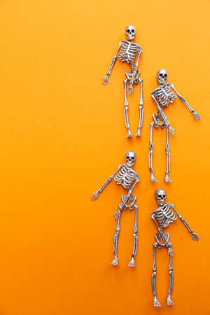 Skeletons in silver and gold are dancing on an orange background. Halloween and Day of the Dead conceptの写真素材