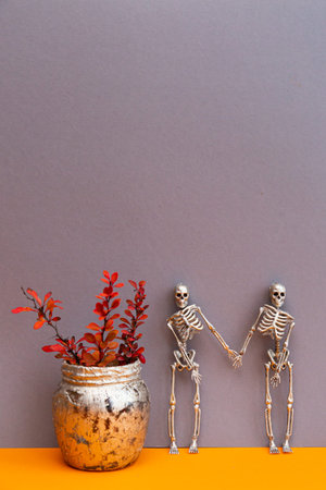 Festive Halloween composition. Skeleton and pink-orange sprigs of barberry on a gray-orange...