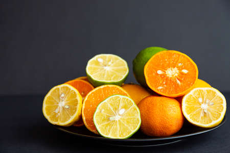 Citrus. Lemons, limes and tangerines whole and halves on black plates on a black background. Healthy food and vitaminsの写真素材