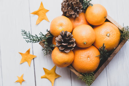Winter minimalistic still life. Tangerines and cones in a wooden box on a light wooden table.の写真素材