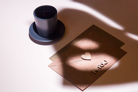 A cup of espresso, an envelope with a heart and the phrase I love you. Monstera palm leaf shadow on the table. Minimalistic valentine's day compositionの写真素材