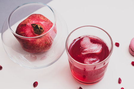 Minimalistic still life with pomegranate fruit and pomegranate juice in a glass glass with an ice cube in the shape of a heart on a light background selective focus top viewの写真素材