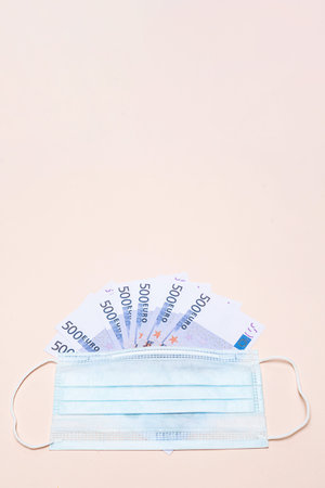 500 euro banknotes and a protective medical face mask on a light background. Health protection and...