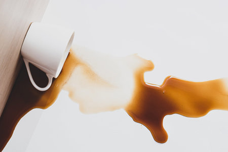 Cup of coffee spilled. Spot of black coffee spilled from a white cup on a light backgroundの写真素材