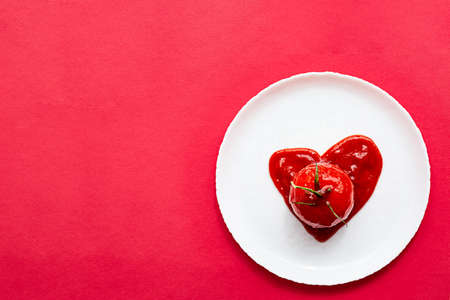 Heart shaped tomato in tomatoes paste, on a white plate. Modern creative still life.の写真素材
