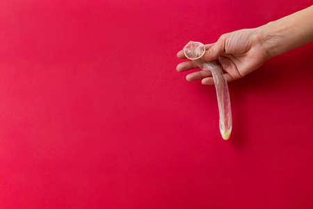 Used condom in female hand. The minimal concept of safe sex on the red background. World AIDS Day.の写真素材