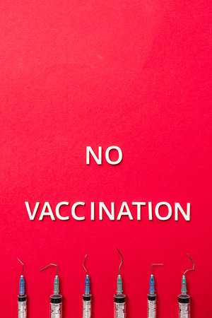 The phrase NO VACCINATION, broken injection syringes on a red background. Stop vaccination concept.