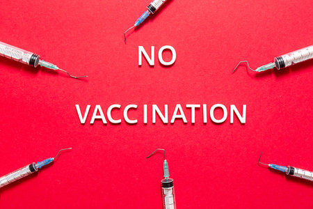 The phrase "NO VACCINATION", broken injection syringes on a red background. Stop vaccination concept.の写真素材
