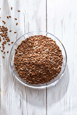 Flax seeds in glass bowl on the white wooden table. Close up and copy space.の写真素材